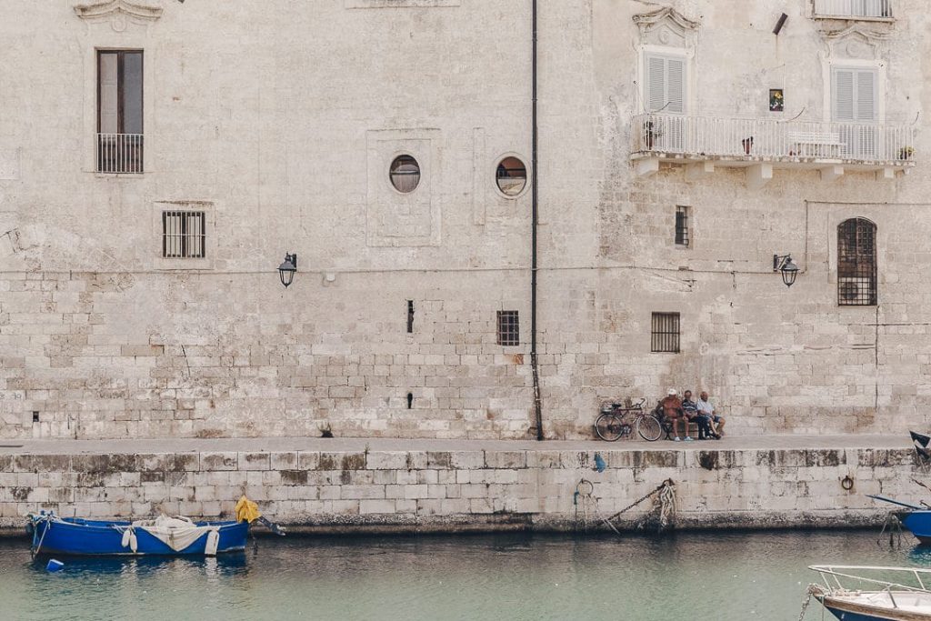 3 hommes discutent à l'ombre dans le port pittoresque de Monopoli dans les pouilles
