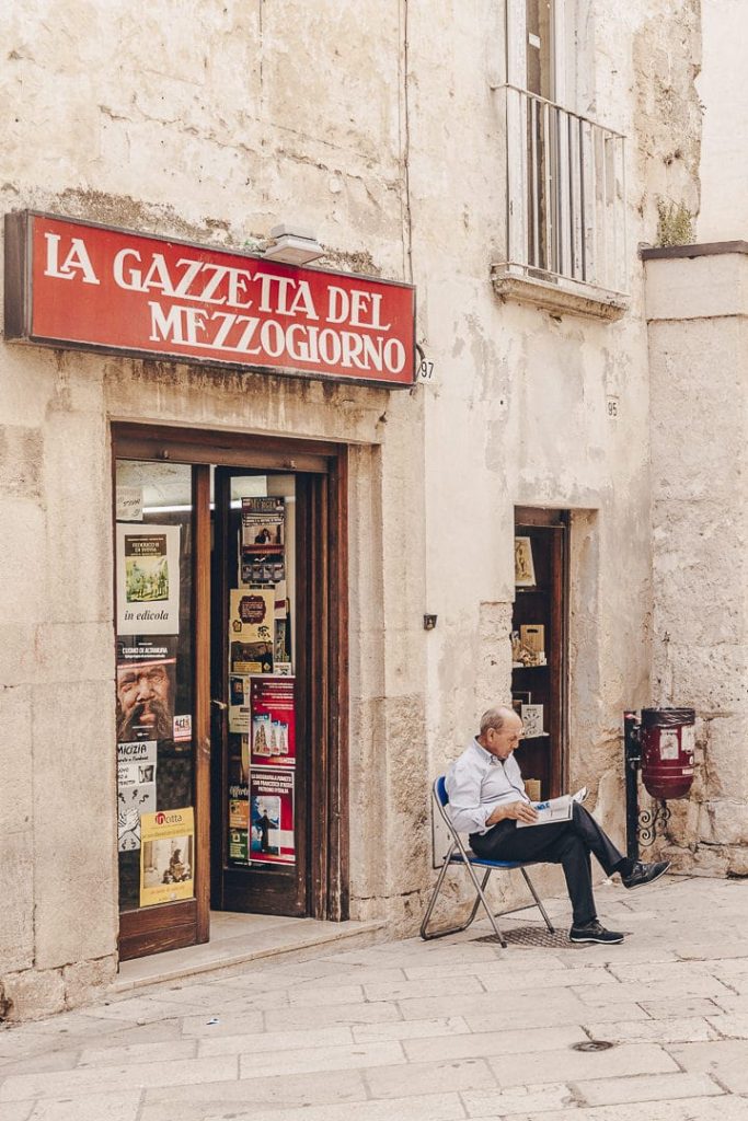 Papi en train de lire le journal devant un magasin de journaux dans un village des Pouilles