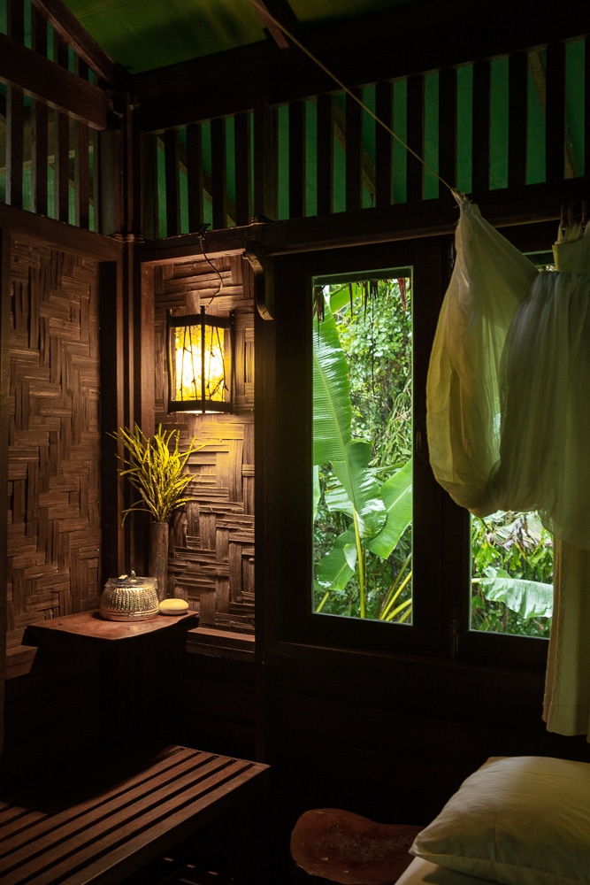 intérieur sombre d'une chambre sur pilotis en bois avec fenetre donnant sur la forêt