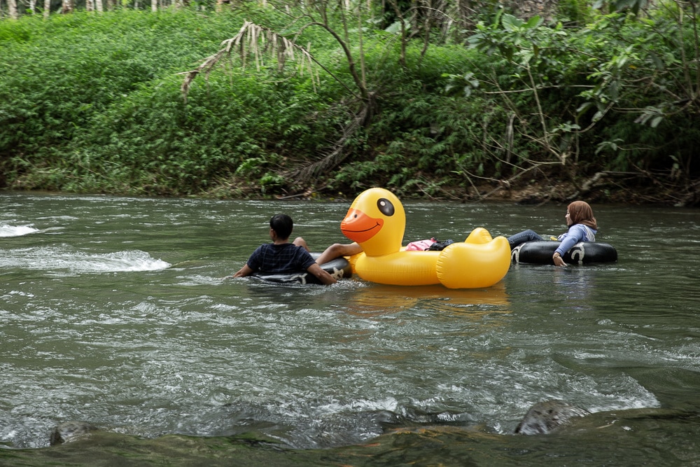 bouée jaune en forme de canard sur une rivière avec deux personnes s'accrochant dessus