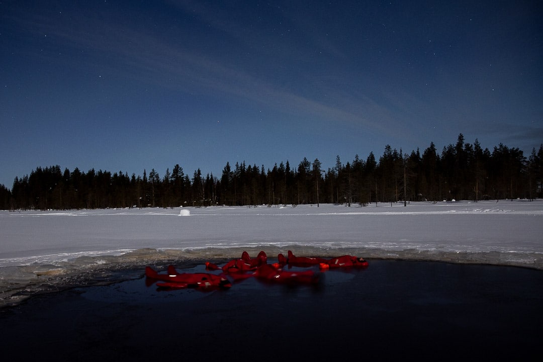 hommes flottant sur un lac gelé sous un ciel étoilé en Lapinie