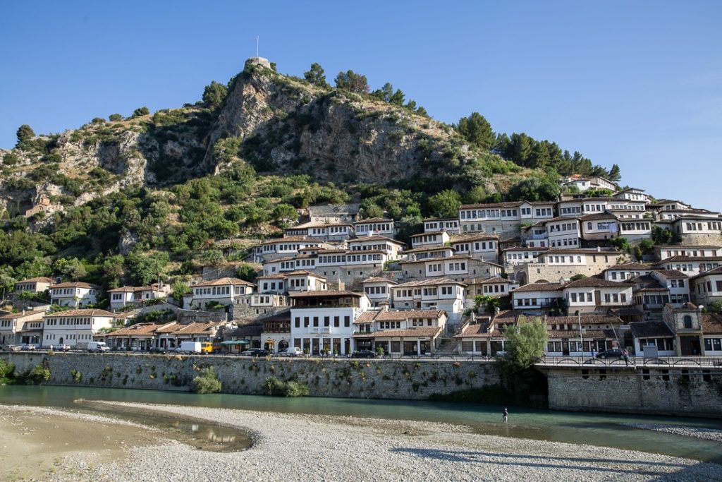 Vue panoramique de la ville de Berat en Albanie, célèbre pour ses maisons ottomanes empilées à flanc de colline, avec une rivière paisible en contrebas. Découvrir ce joyau classé à l’UNESCO est une excellente raison de louer une voiture en Albanie et explorer librement ses paysages authentiques.