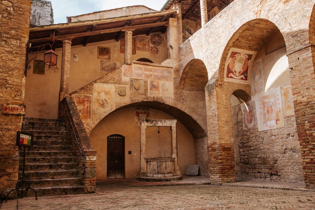 Cour de la médiévale San Gimignano qui permet d'entrer dans les musées civiques. Elle est décorée de fresques et d'un escalier couvert