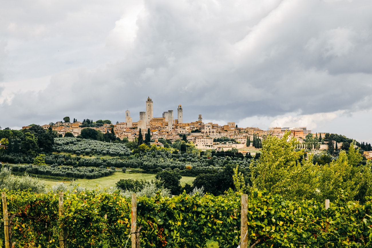 ville de San Gimignano et ses tours médiévales avec en premier plan des vignes, sous un ciel nuageux
