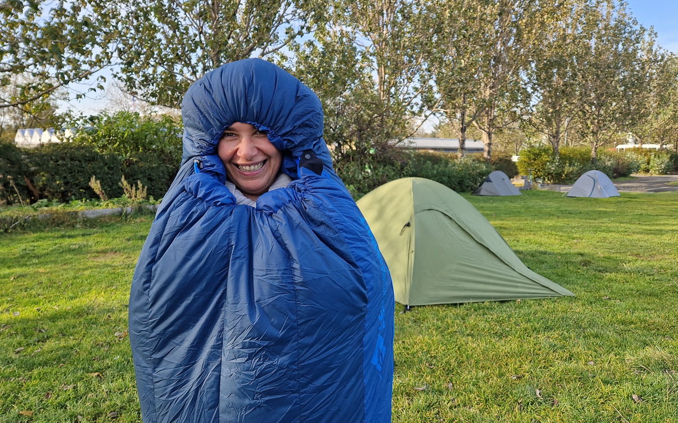 personne souriante dans un duvet devant une tente de camping